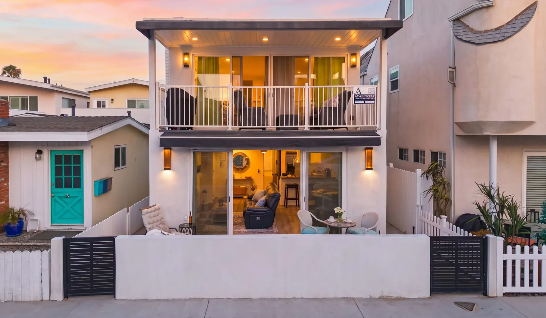 Una casa de dos pisos tiene un balcón sobre un patio al atardecer.