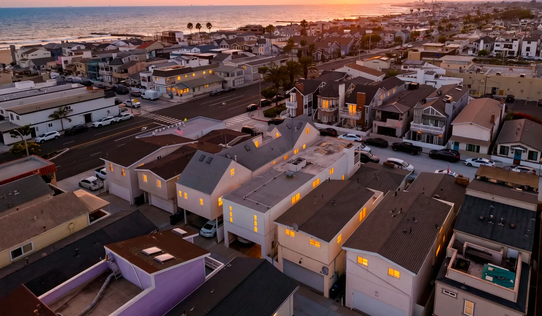 Vista aérea de un barrio costero al atardecer, con el océano en el horizonte.