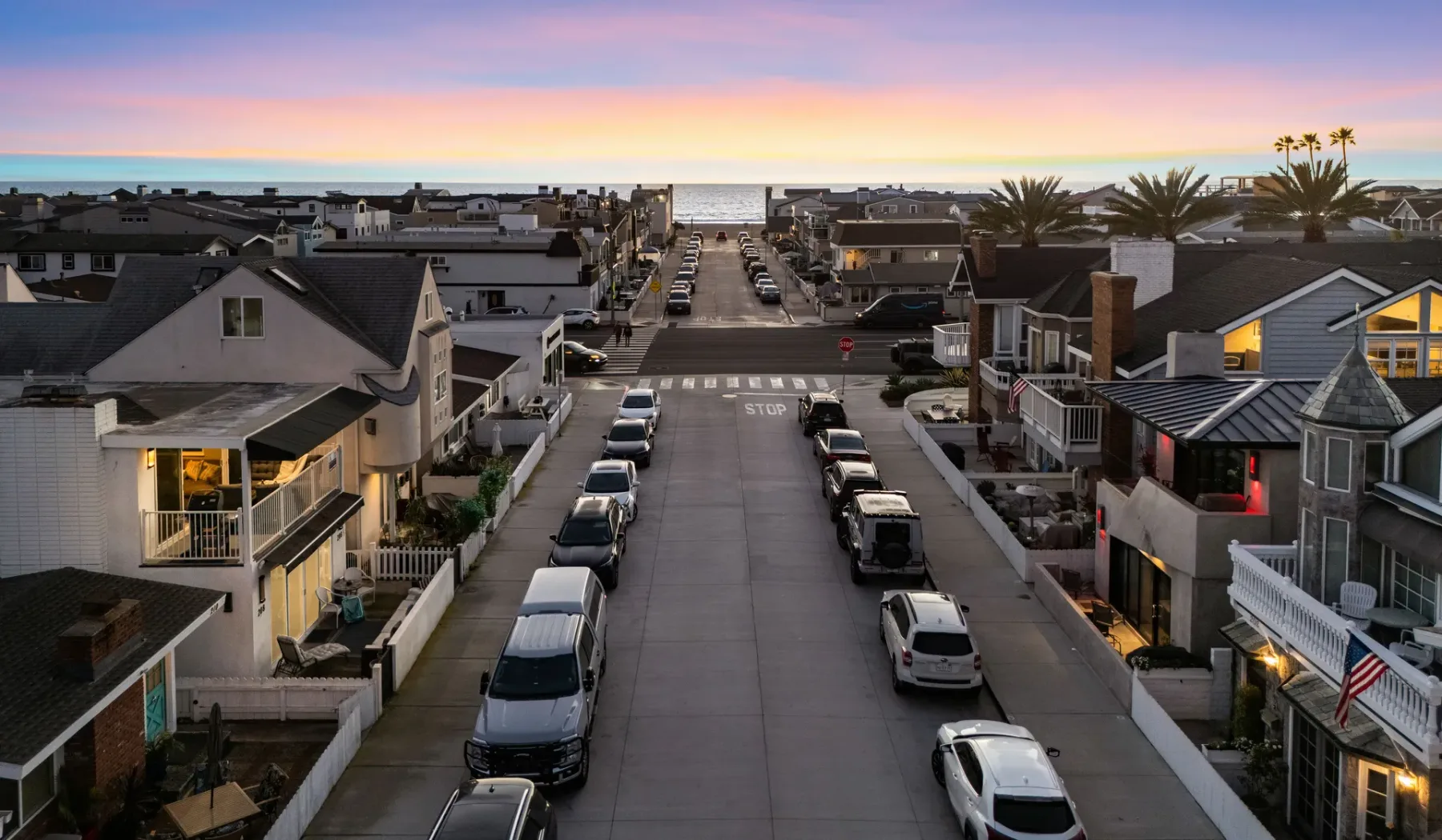 Una calle residencial conduce hacia el océano bajo un cielo colorido al atardecer.