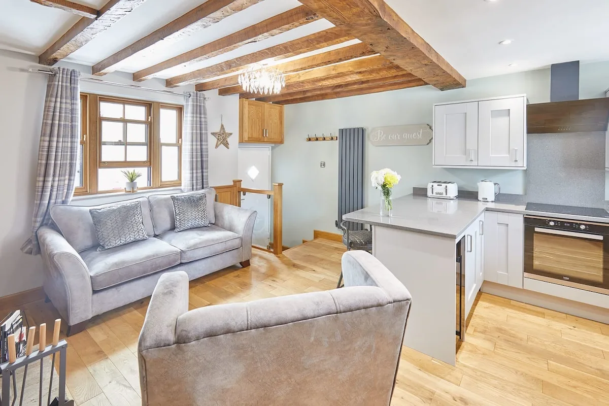 Una sala de estar y cocina de planta abierta con asientos bajo vigas de madera expuestas.