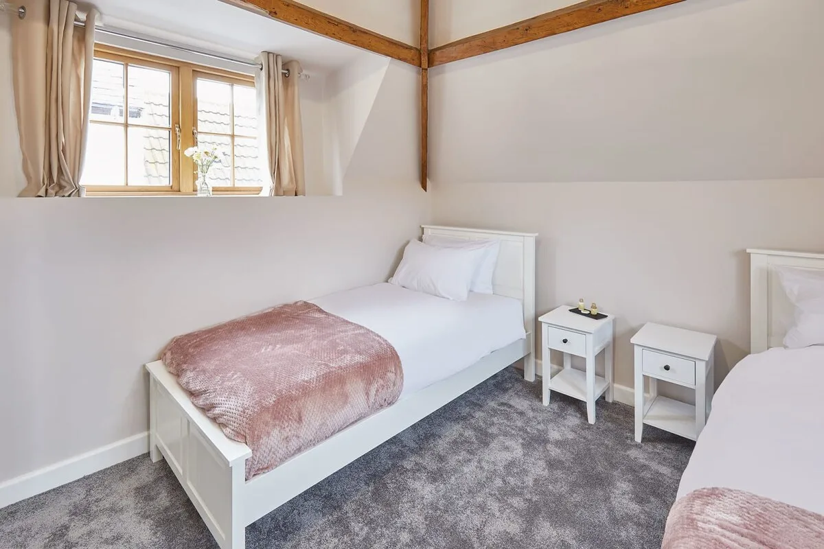 Un dormitorio luminoso con dos camas, mesitas de noche y una ventana.