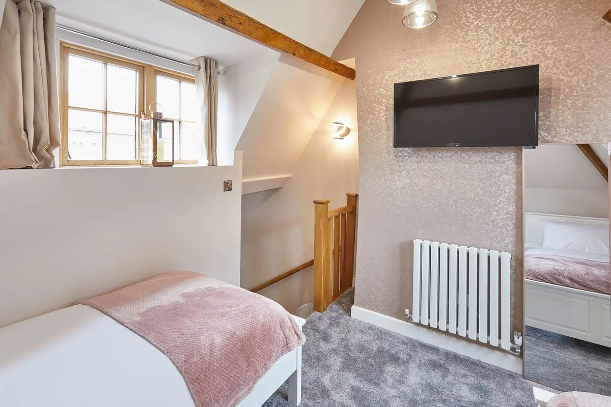 Un dormitorio con una cama, un televisor montado en la pared y una ventana junto a las escaleras.