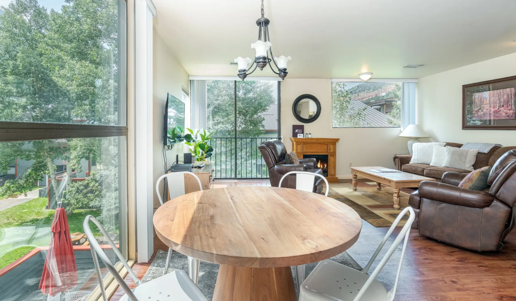Una luminosa sala de estar y comedor con grandes ventanas y una mesa redonda de madera.