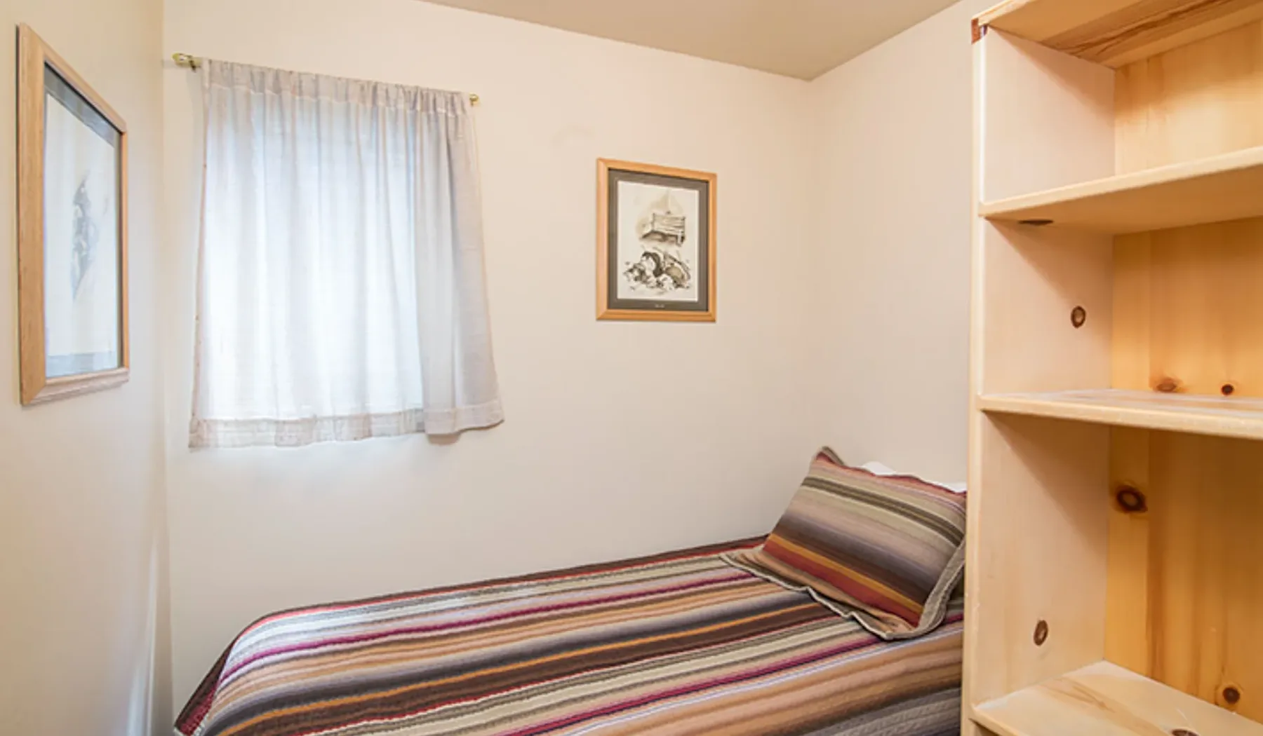 Un dormitorio con una cama individual cubierta por una manta a rayas y una ventana con cortinas.