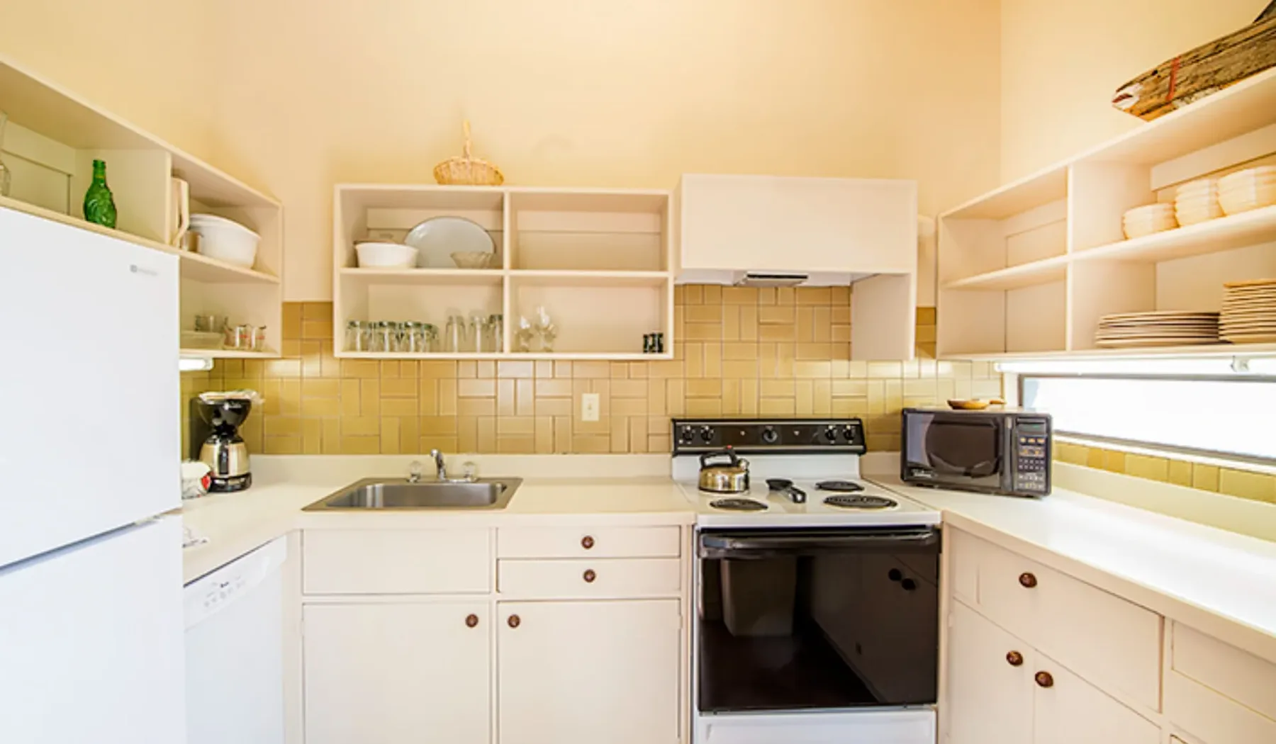 Una cocina luminosa con gabinetes blancos, refrigerador y estufa.
