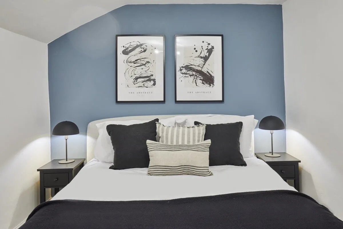 Un dormitorio con una cama bien tendida, cojines decorativos y cuadros enmarcados.