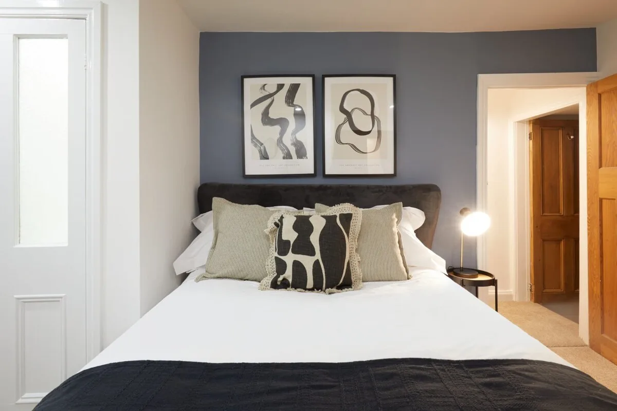 A bedroom with a neatly made bed beneath two framed abstract prints.
