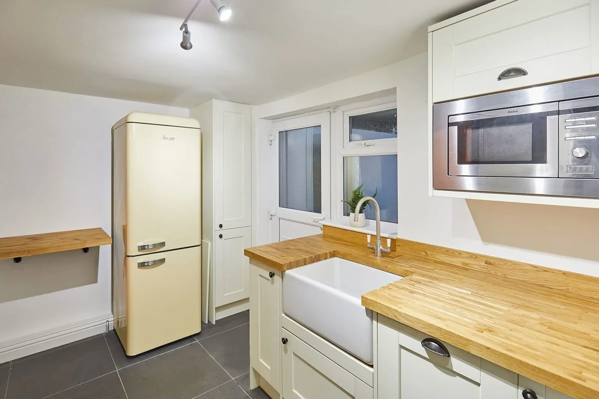 A bright kitchen with wooden countertops, a sink, and a refrigerator.