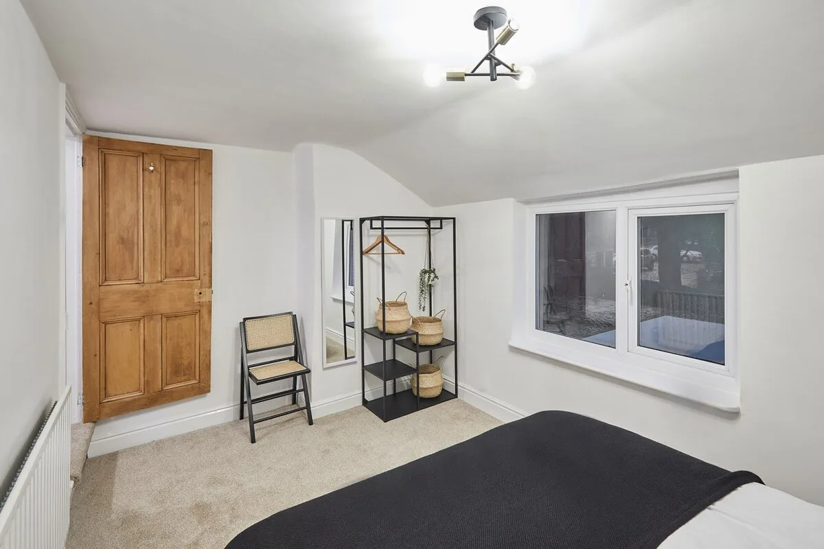 A bright bedroom with a bed, storage rack, and windows.