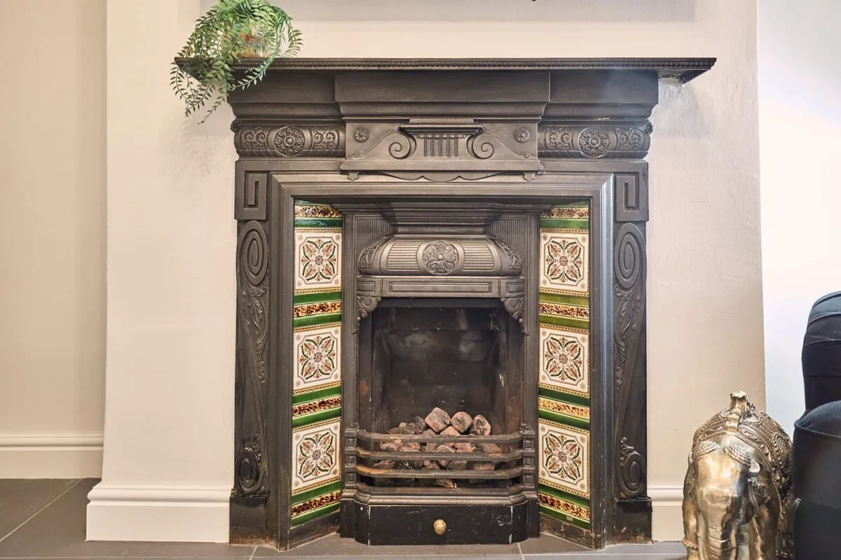 A decorative fireplace with patterned tiles and a small plant above.