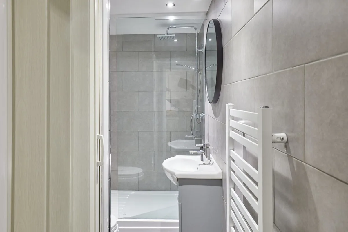A tiled bathroom with a sink, shower, and wall-mounted towel rail.