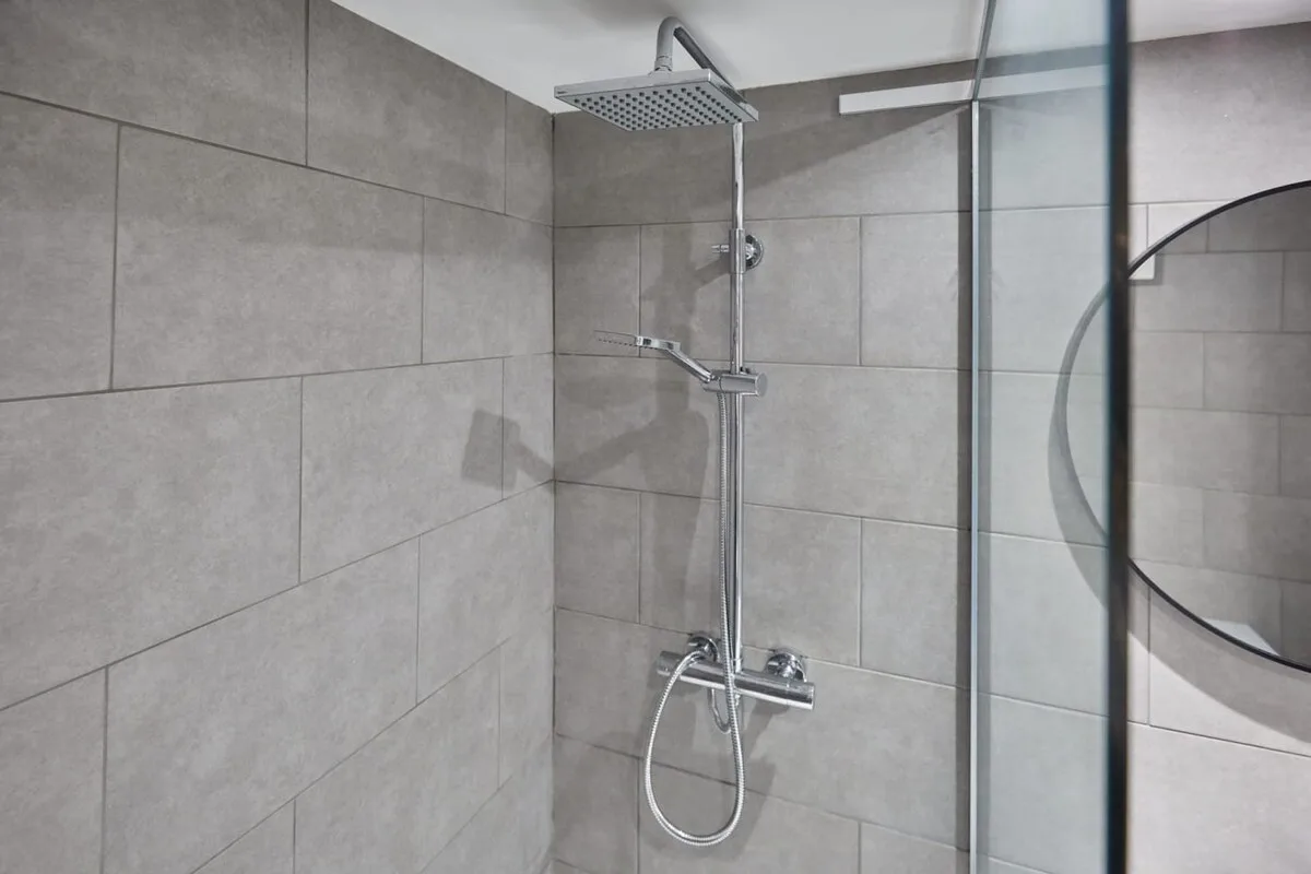 A tiled shower with a rainfall showerhead and handheld spray.