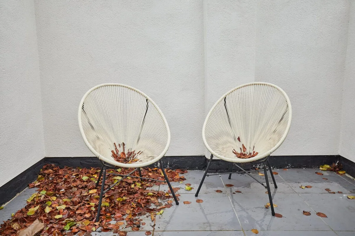 A small patio with two wire chairs and scattered fallen leaves.