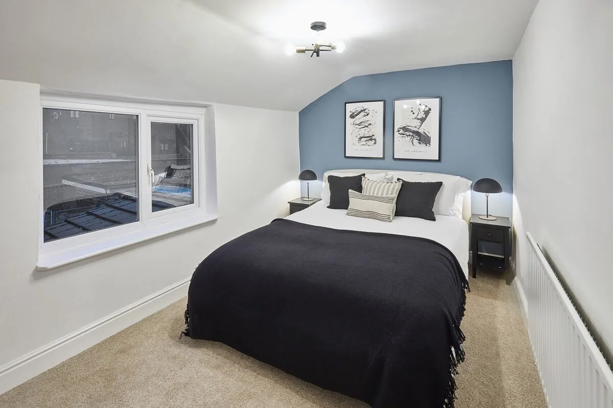 A bedroom with a bed beneath framed artwork and a large window.