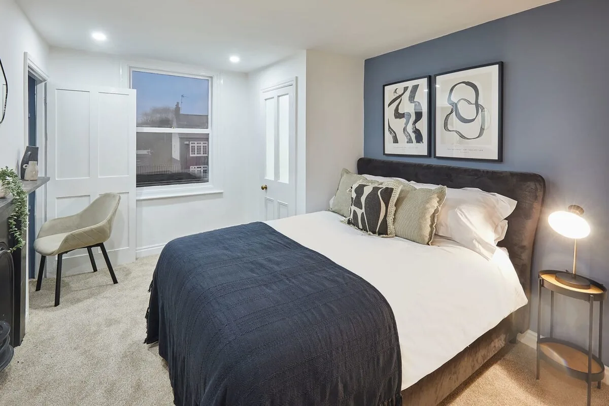 A bedroom with a bed dressed in white bedding and a dark blue blanket.