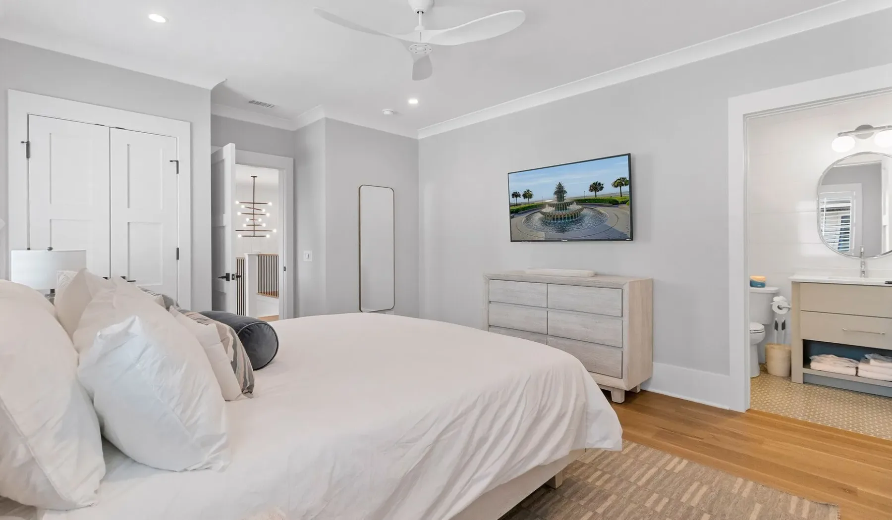 Un dormitorio luminoso con una cama, una cómoda y una puerta abierta al baño.