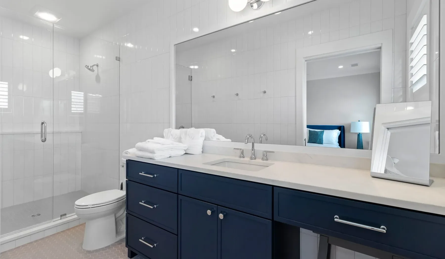 Un baño luminoso con azulejos, ducha de vidrio, inodoro y tocador oscuro.