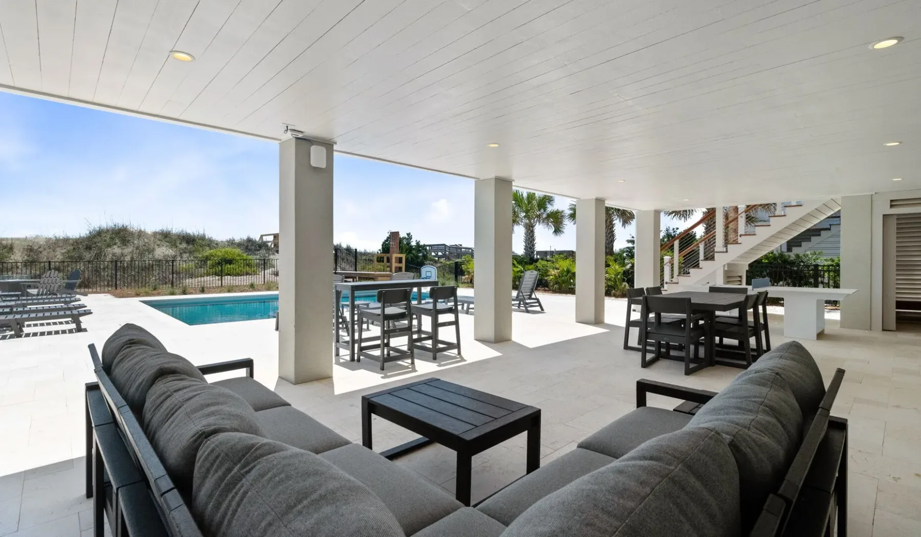 Una sala exterior cubierta con asientos acolchados y una piscina cercana.