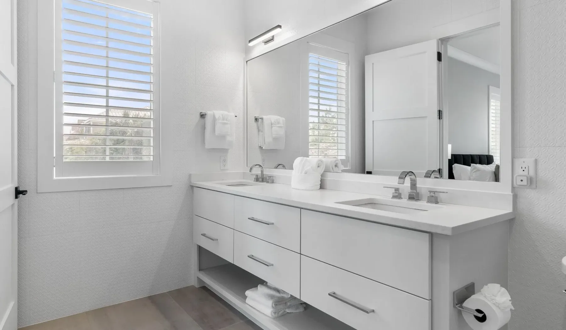 Un baño luminoso con un lavabo largo, espejo y ventana.
