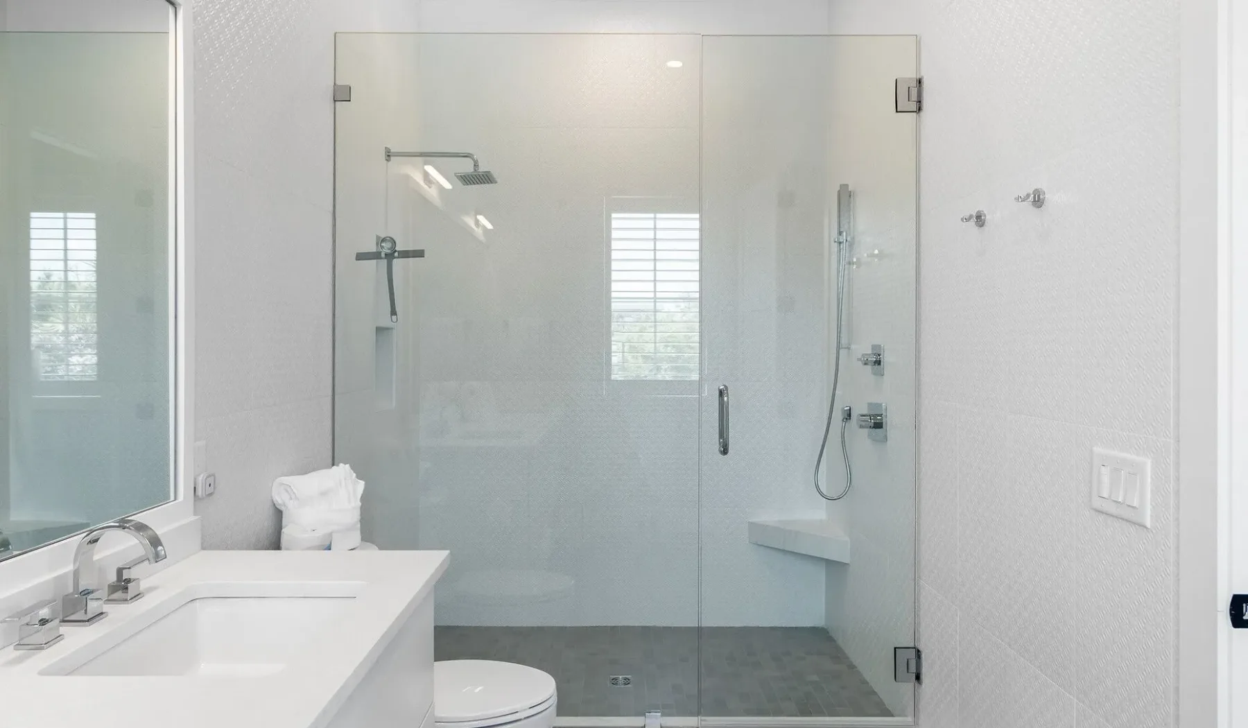Un baño luminoso con una ducha de vidrio y un tocador blanco con lavabo.
