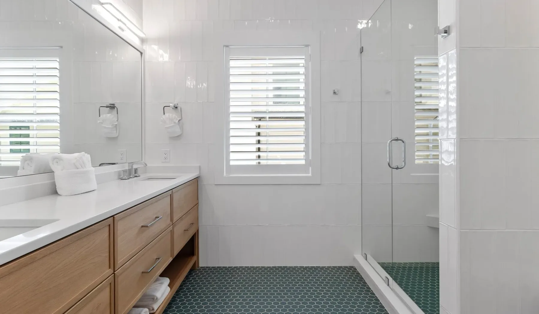 Un baño luminoso con un tocador largo, espejos y una ducha de vidrio.