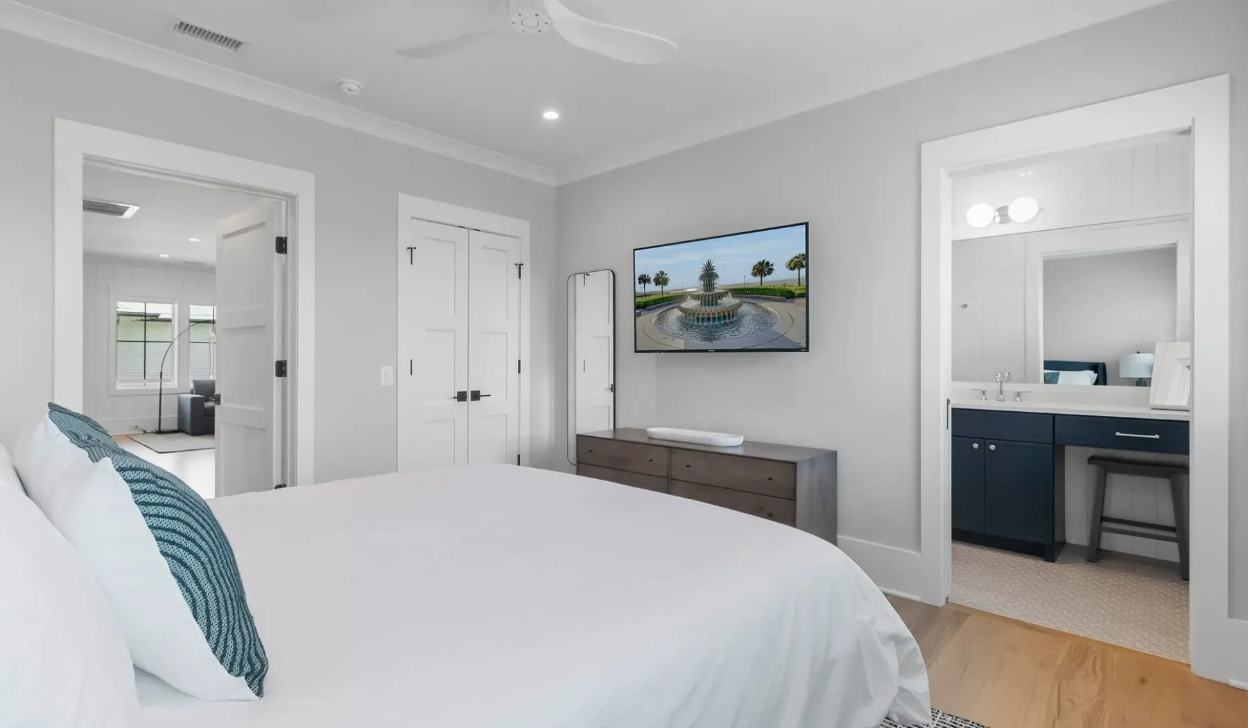 Un dormitorio luminoso con una cama bien tendida y un televisor en la pared.