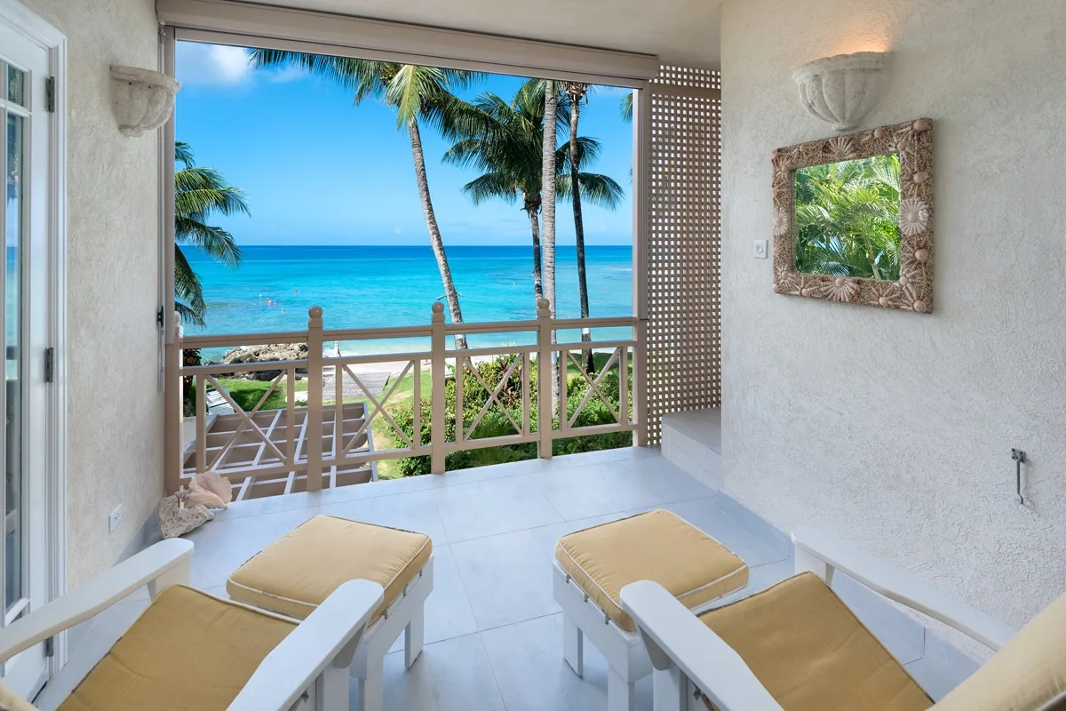 A balcony seating area overlooks palm trees, turquoise water, and the ocean.