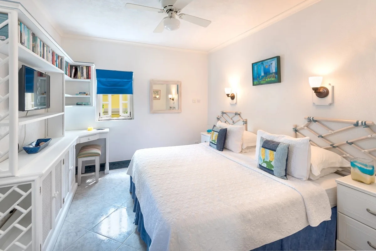 A bright bedroom with two beds, white bedding, and built-in shelving.