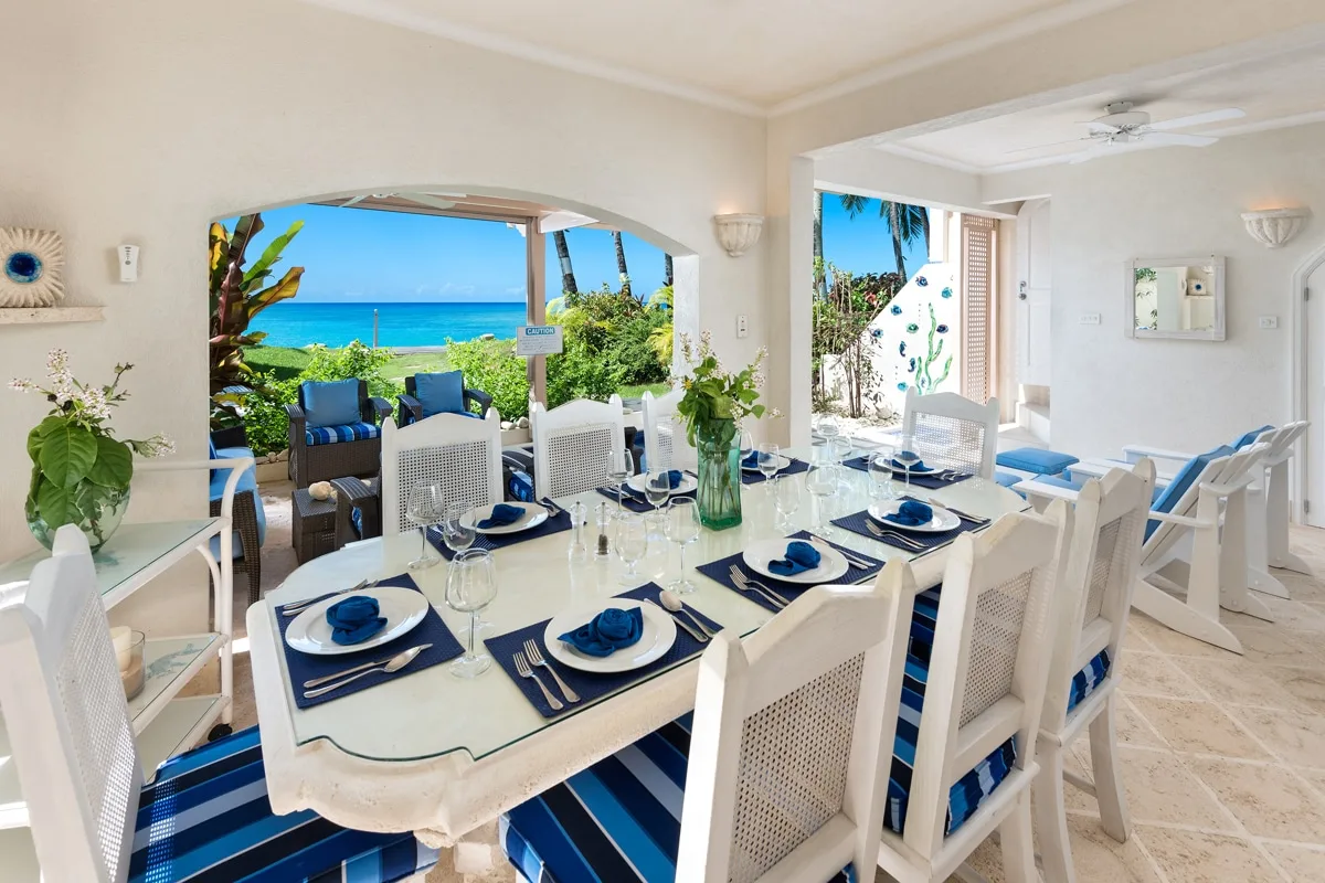 A bright dining area opens onto a patio with tropical greenery and ocean views.