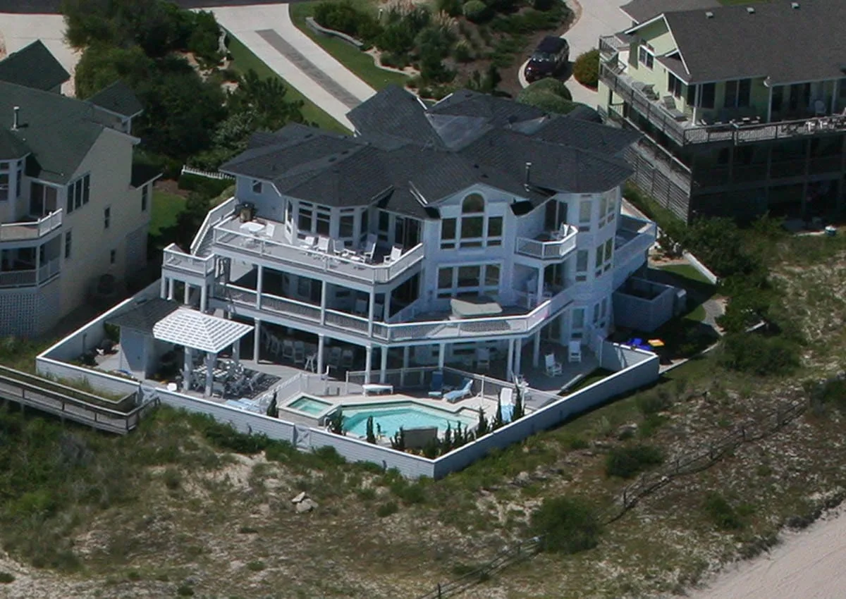 Vista aérea de una gran casa junto al mar, con balcones y una piscina.