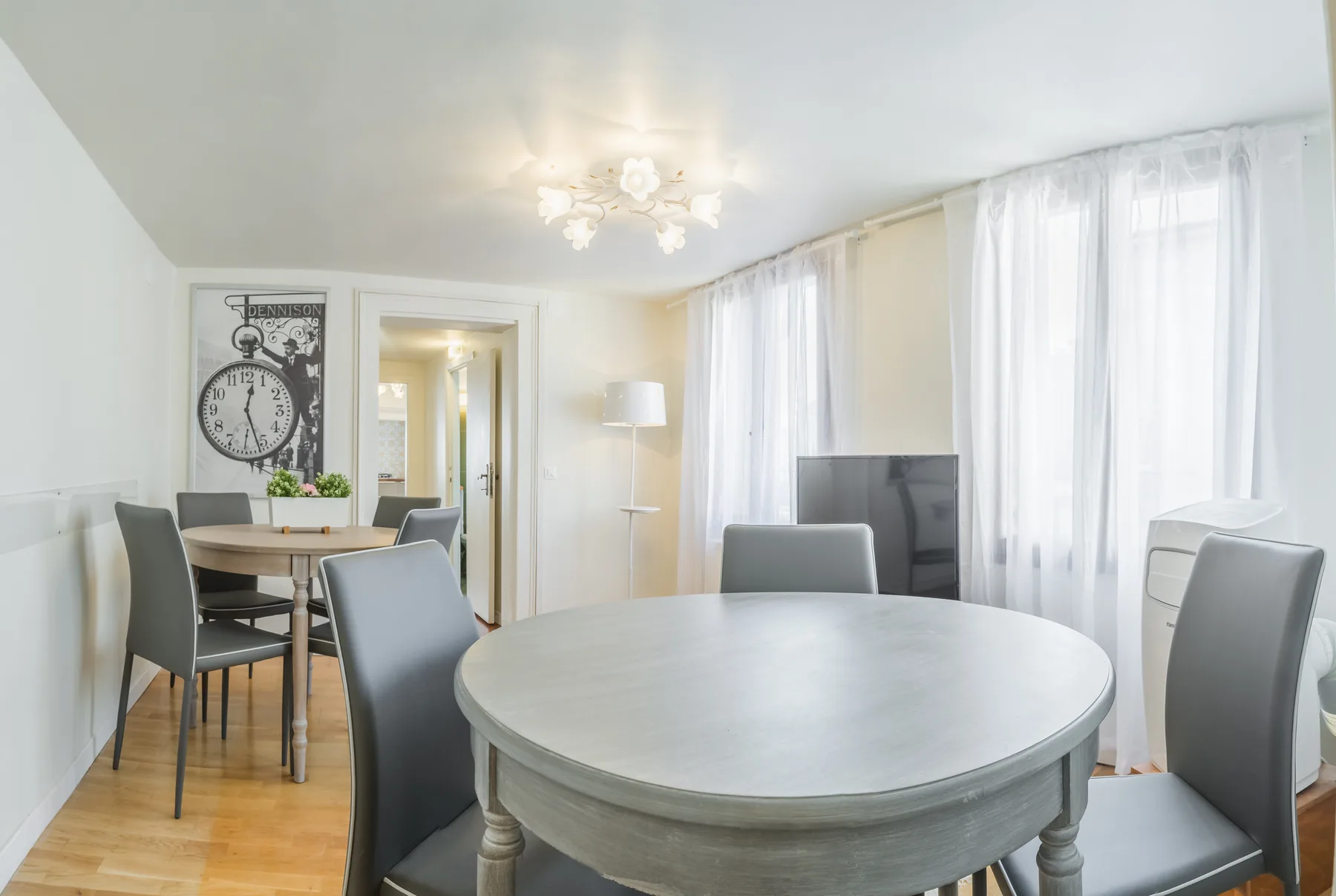 Un comedor luminoso con una mesa redonda y sillas junto a altas ventanas con cortinas.