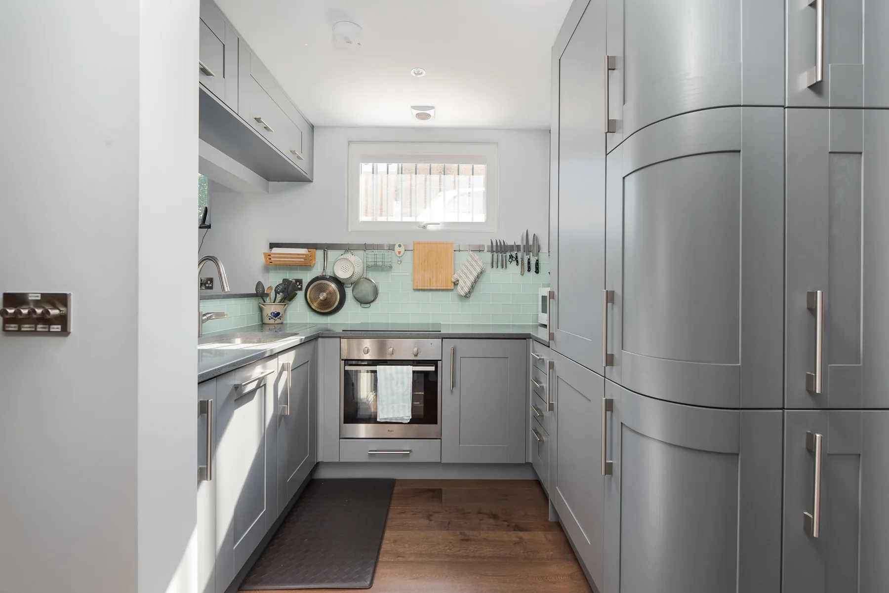 A bright kitchen with gray cabinets, a countertop, and a built-in oven.
