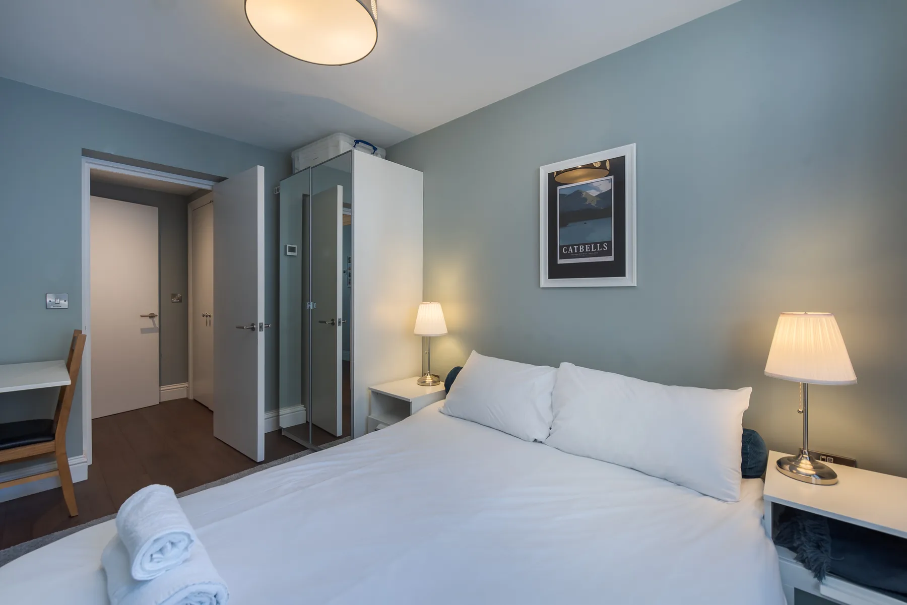 A bedroom with a large bed, bedside tables, and a desk beside the doorway.