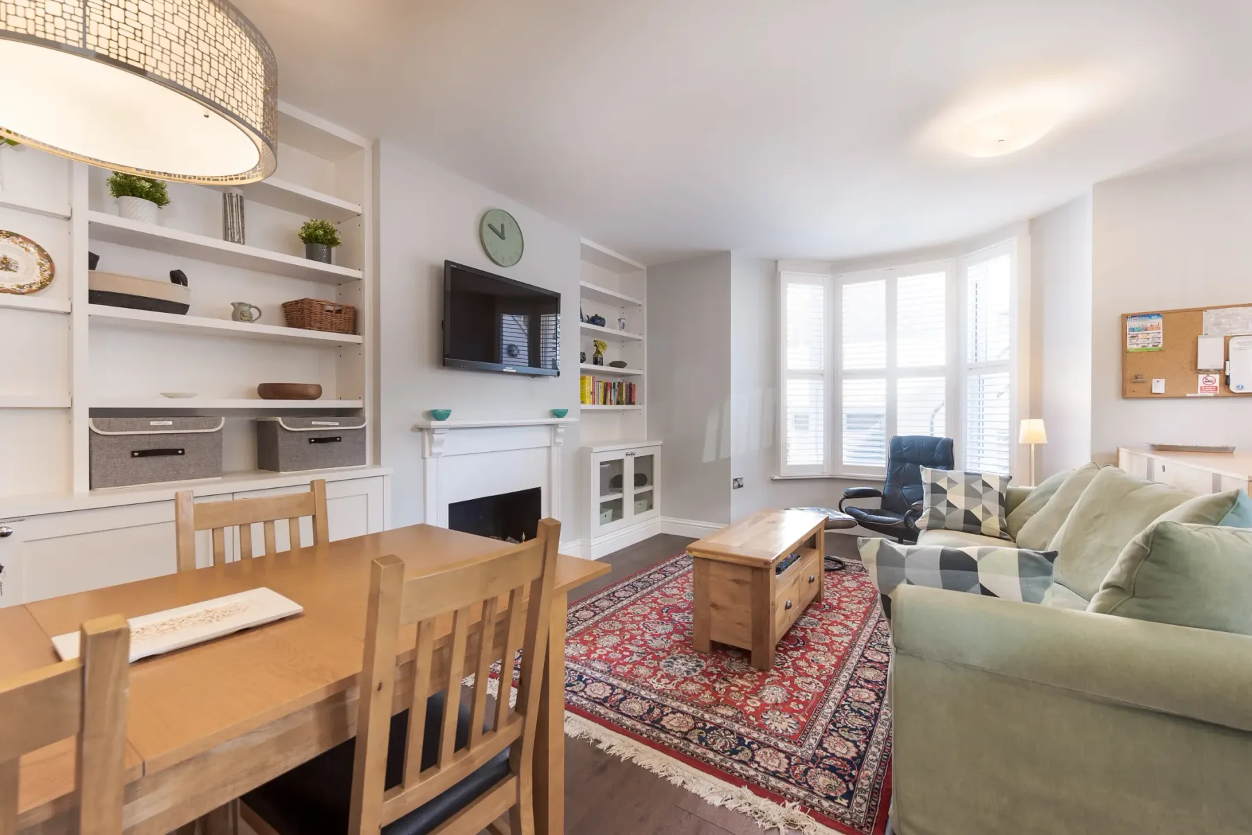 A bright living room with a dining table, seating, and a patterned rug.