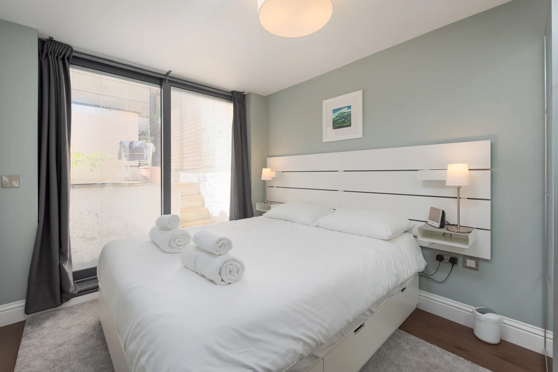 A bedroom with a large white bed beside a tall window.
