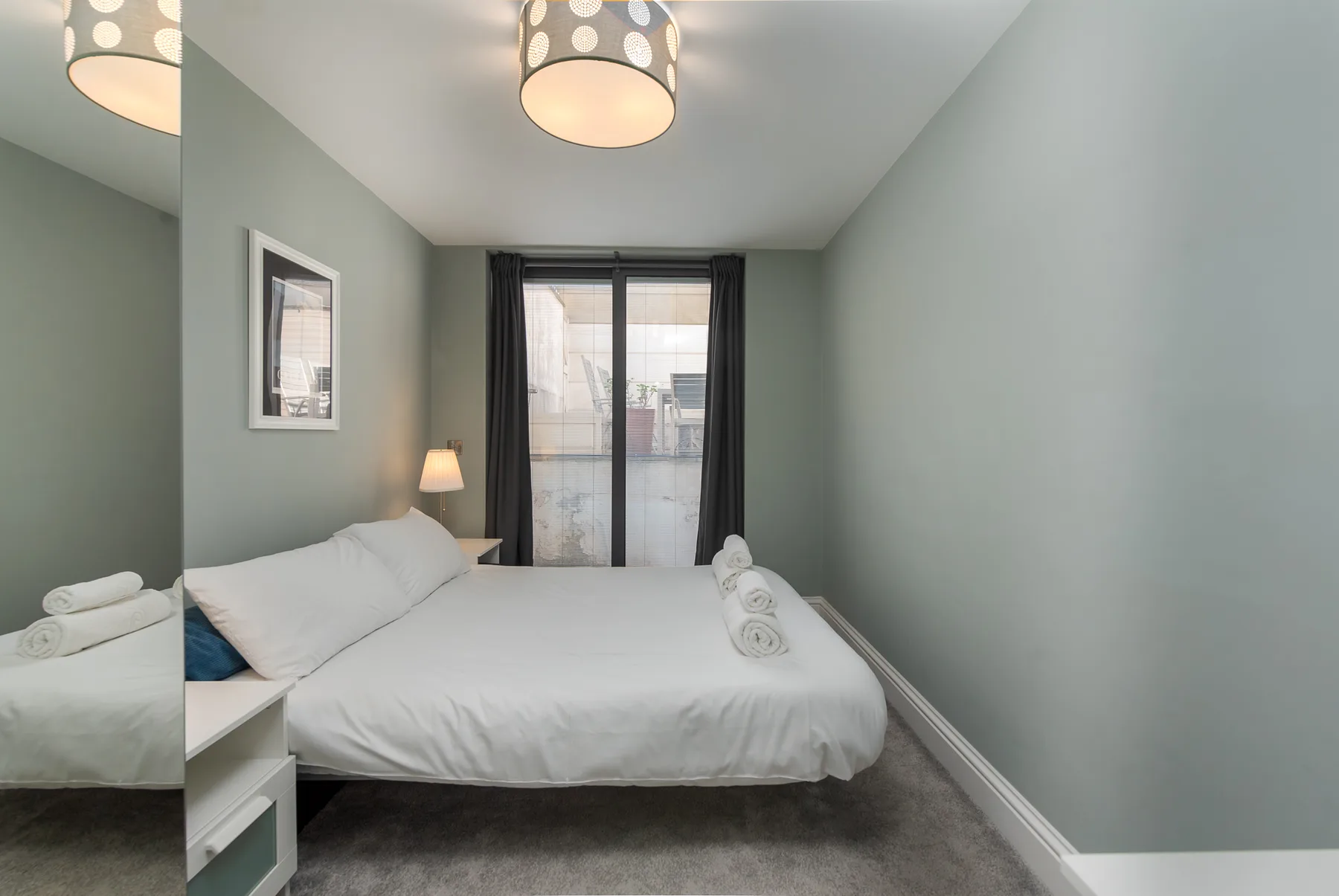 A bedroom with a neatly made bed and a window framed by dark curtains.