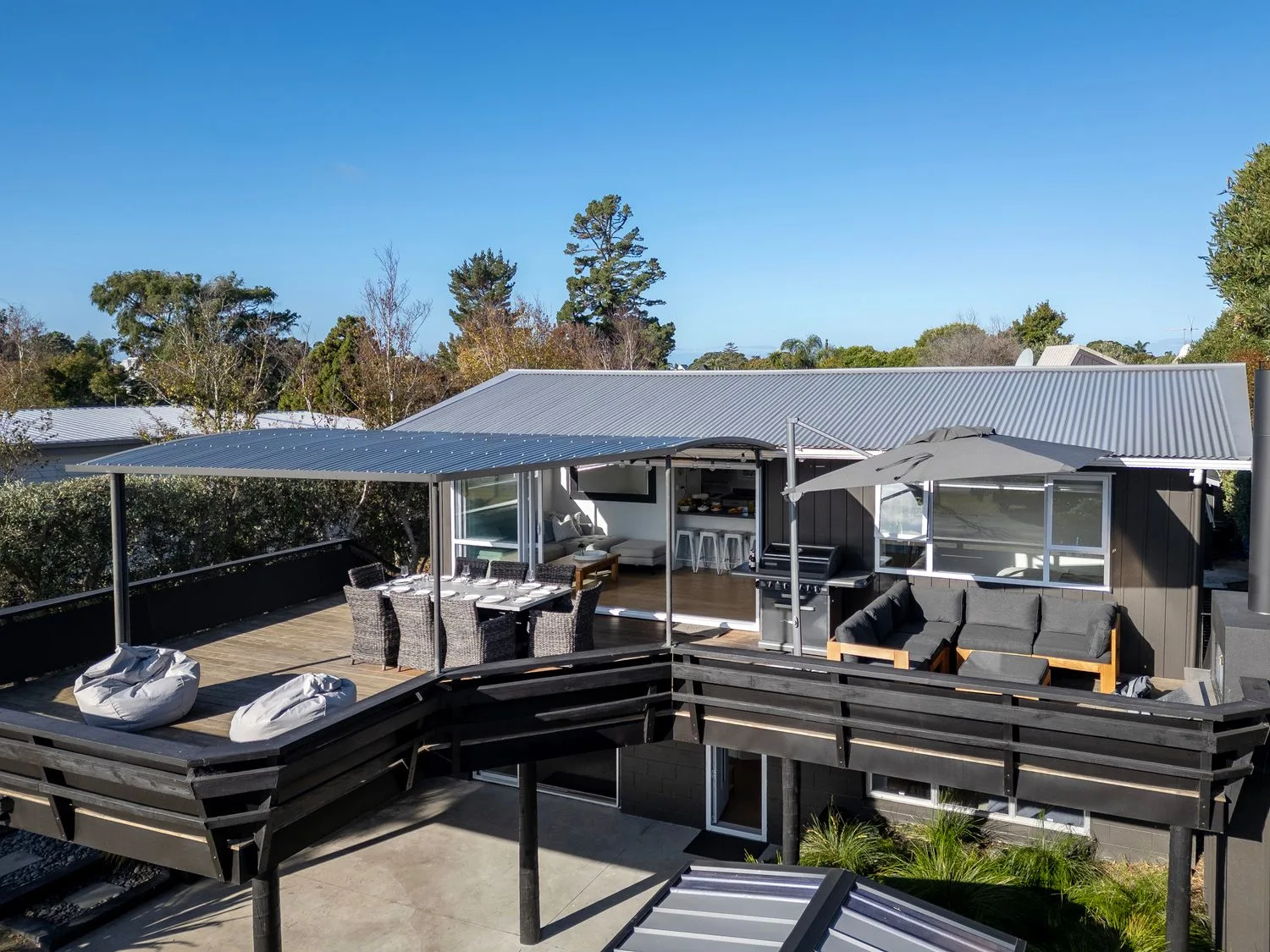 Una terraza exterior con mesa y sillas de comedor bajo techo y una zona de estar con sombrilla en Sol Vista Paku - Pauanui Holiday Home, en Pauanui