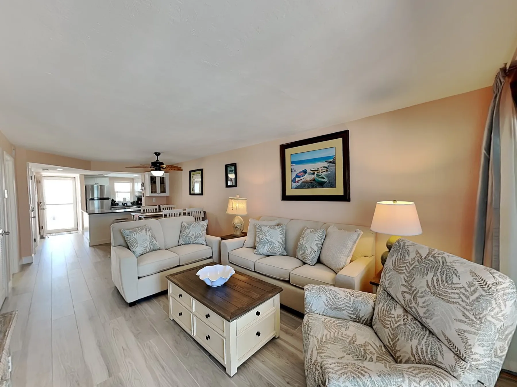 A living room with seating, a coffee table, and an open kitchen beyond.