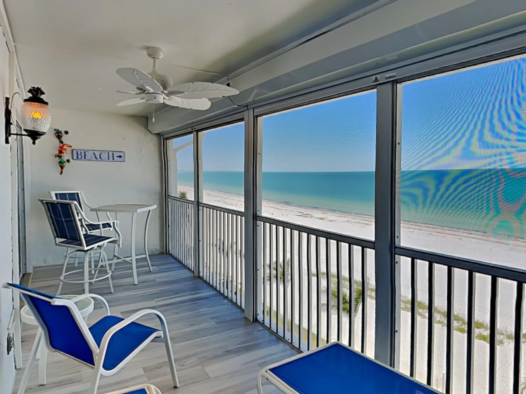 A balcony with blue seating overlooks the beach and ocean.