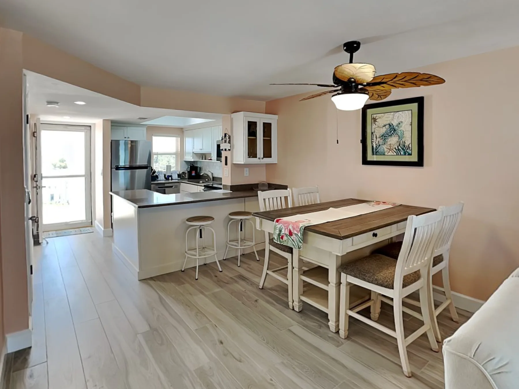 An open-plan dining area and kitchen with a wooden dining table and ceiling fan.