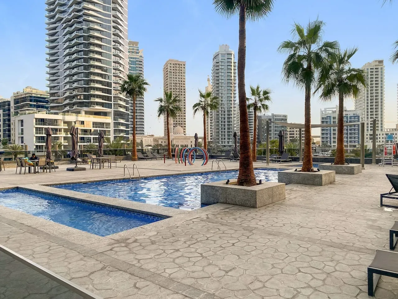 An outdoor pool sits among palm trees and high-rise buildings.
