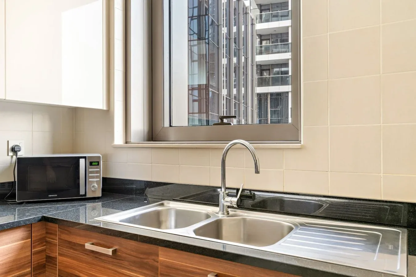 A kitchen counter with a double sink sits beneath a large window.