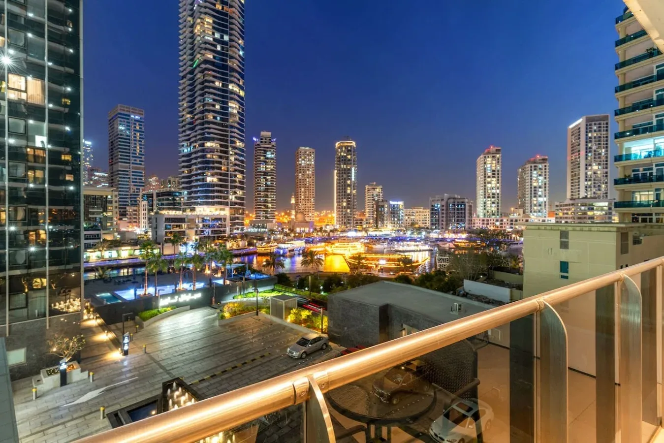 A nighttime city skyline with illuminated high-rise buildings viewed from a balcony.