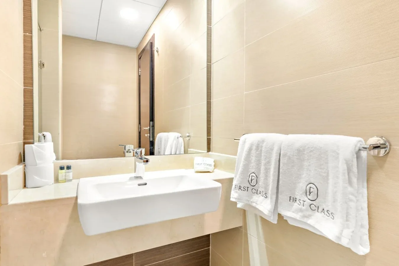 A tiled bathroom vanity with a sink, mirror, and folded towels.