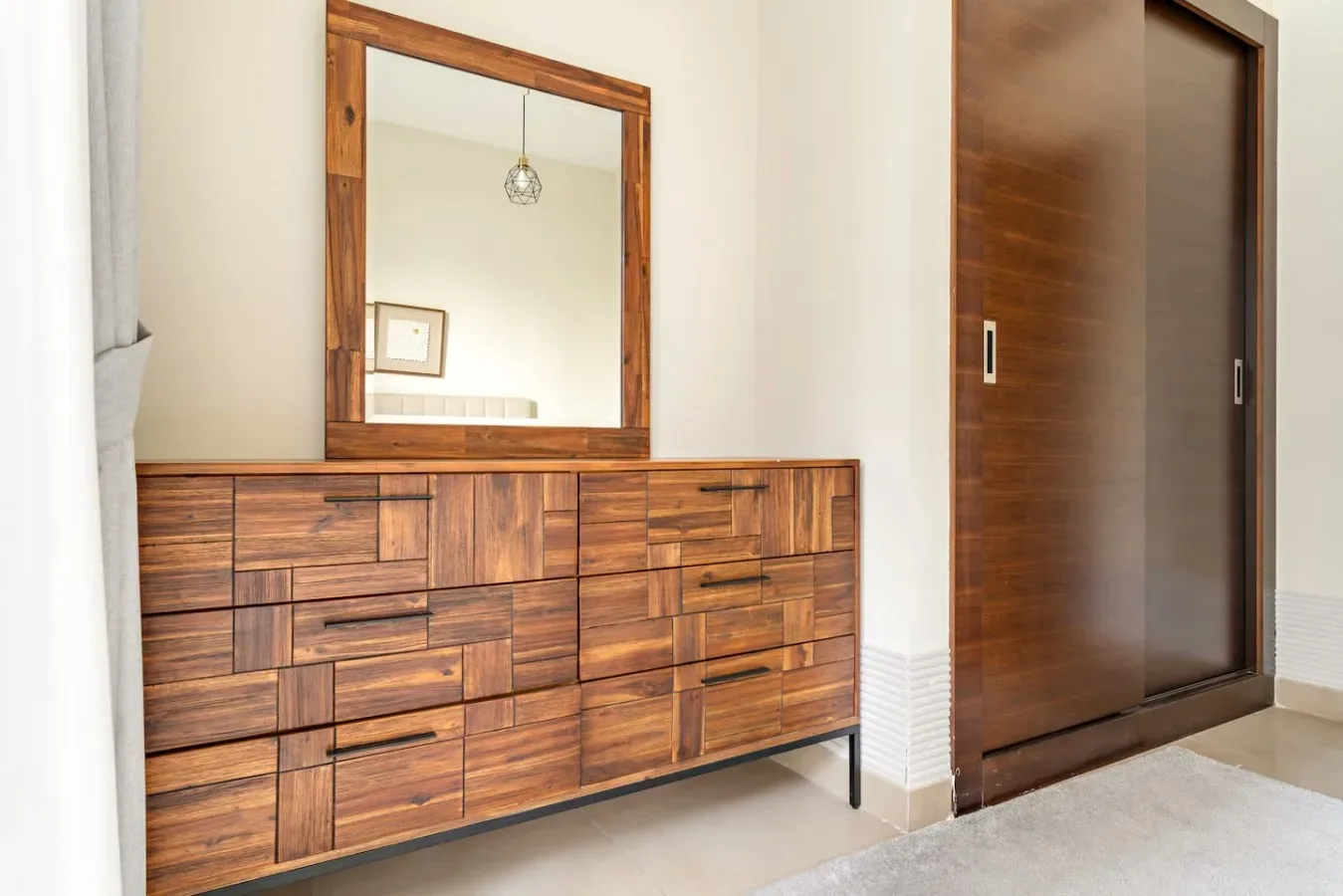 A wooden dresser with a framed mirror stands beside a sliding door.