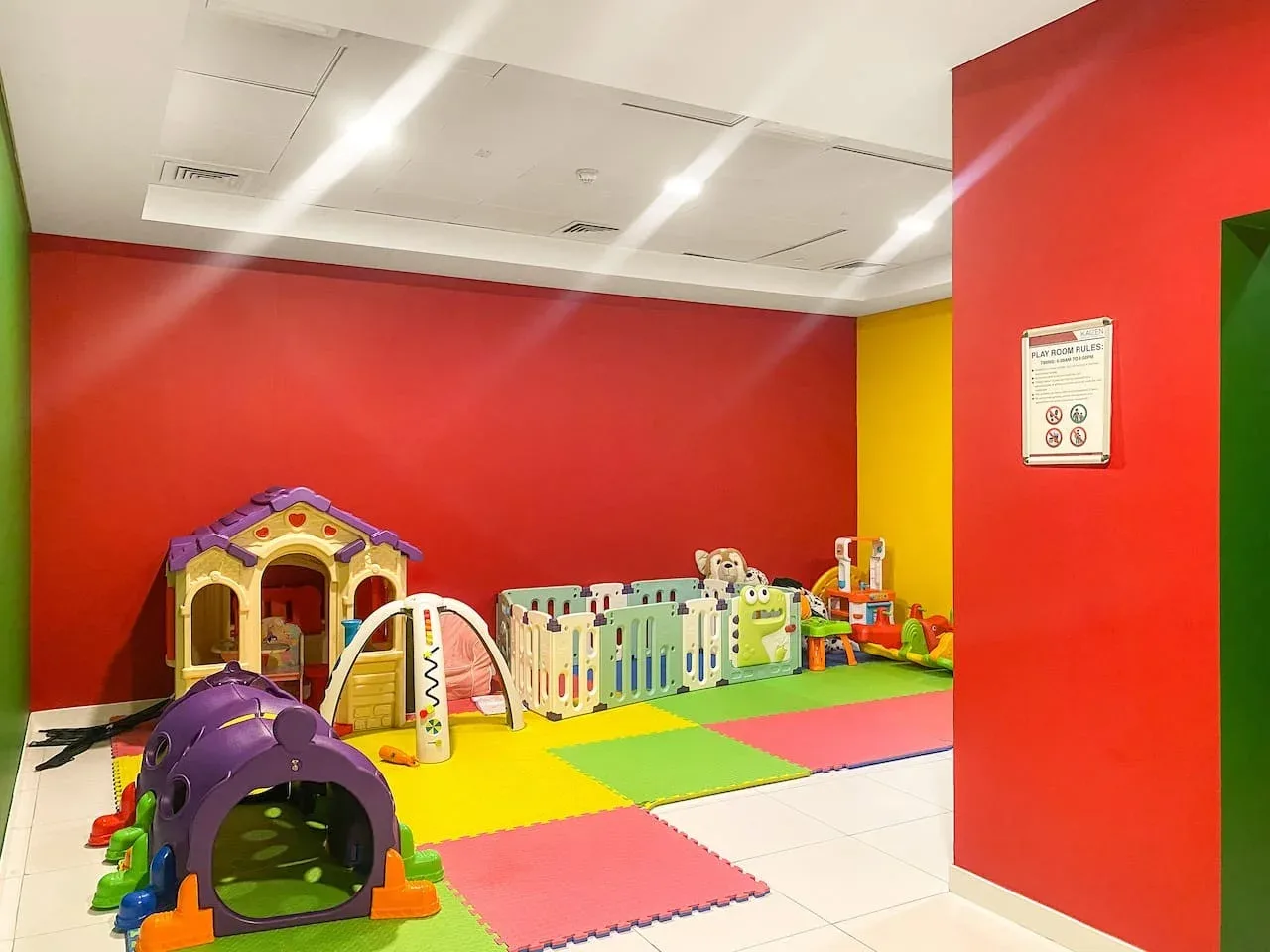 A colorful indoor play area has soft mats, a play tunnel, and children’s play equipment.
