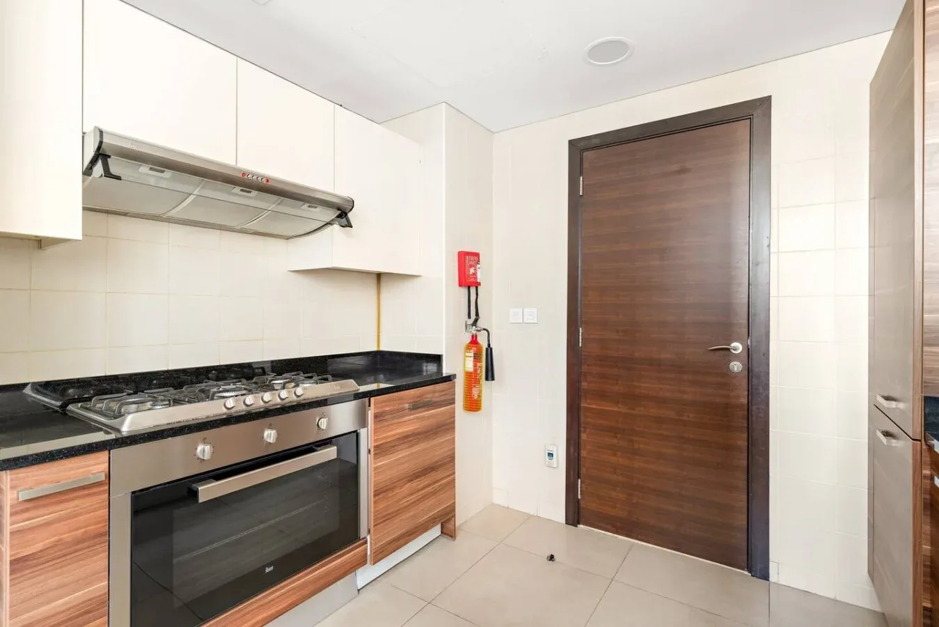 A modern kitchen with a cooktop, oven, and a wooden door.