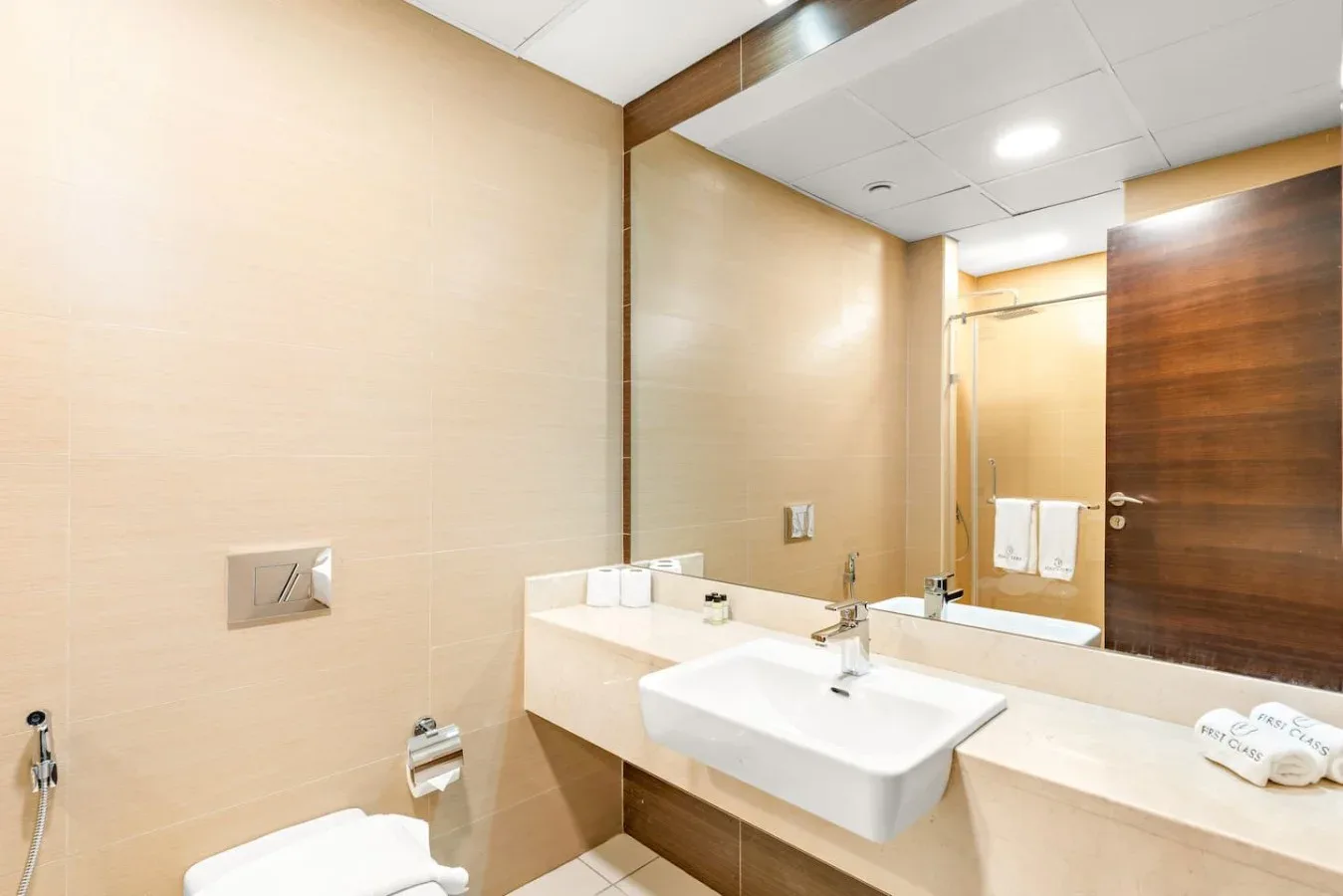 A bathroom with a sink, a wide mirror, and beige tiled walls.