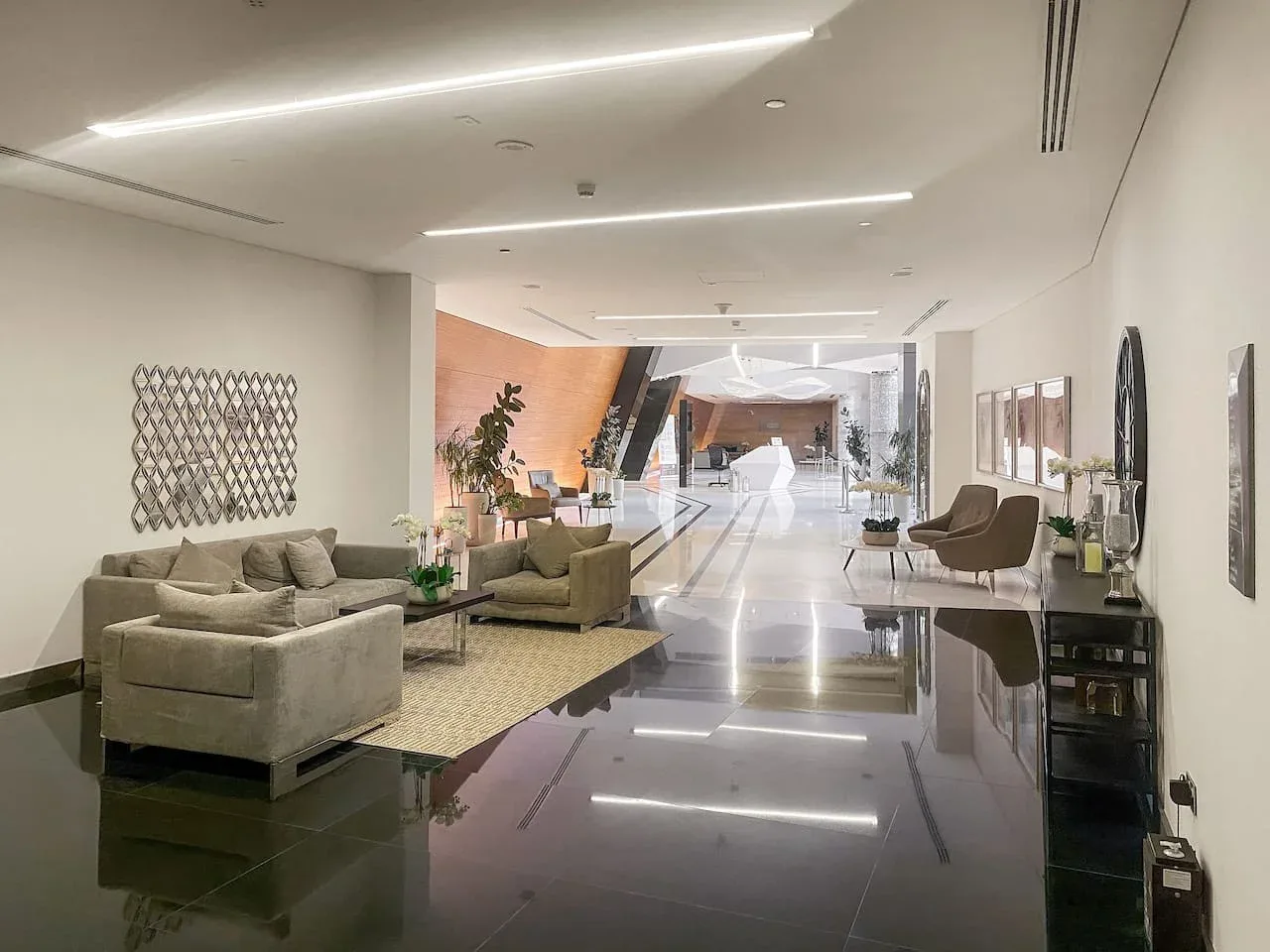 A modern interior lounge with seating and a bright hallway extending into the background.