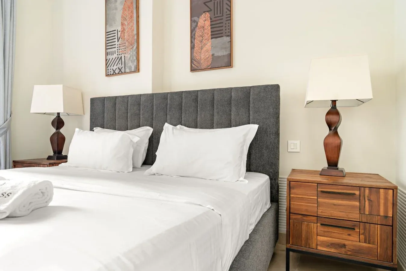 A bedroom with white bedding, a dark upholstered headboard, and wooden bedside tables.